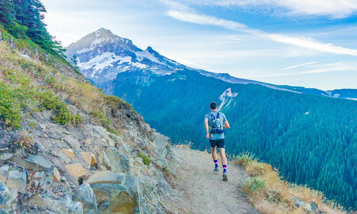 Coureur de trail sur un sentier de crête face à une montagne enneigée