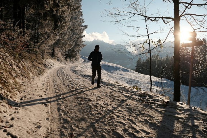 Personne qui court sur un chemin enneigé en forêt, face au soleil bas