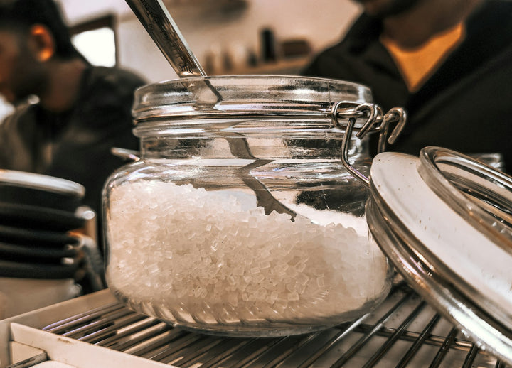 Pot en verre rempli de sucre blanc avec une cuillère, sur un comptoir de cuisine
