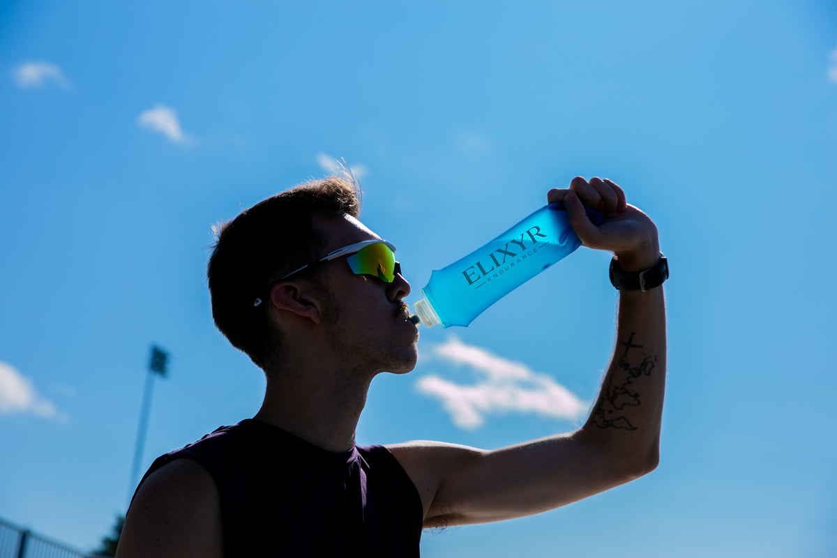 Athlète buvant dans une gourde souple ELIXYR sous un ciel bleu